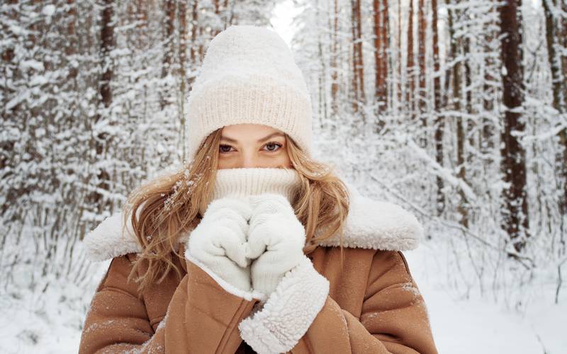 Les bienfaits de la marche pour la peau. Promenade d'hiver, une belle blonde en vêtements d'hiver marchant dans une forêt enneigée, une belle journée gelée. Une jeune femme qui se réchauffe le nez enveloppé d'une écharpe blanche. Cabinet du Docteur Dominique DENJEAN à PARIS 2.